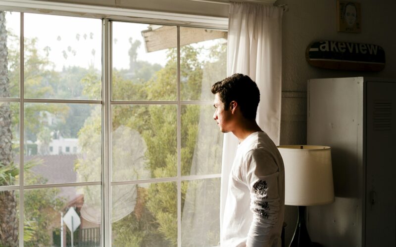 Persona mirando por una ventana en un departamento minimalista, luz natural tenue