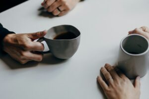 Slow dating: por qué las citas lentas están ganando terreno frente al scroll infinito Dos personas conversando con tazas de café en una mesa, ambiente cálido y tranquilo