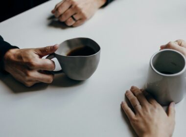 Dos personas conversando con tazas de café en una mesa, ambiente cálido y tranquilo