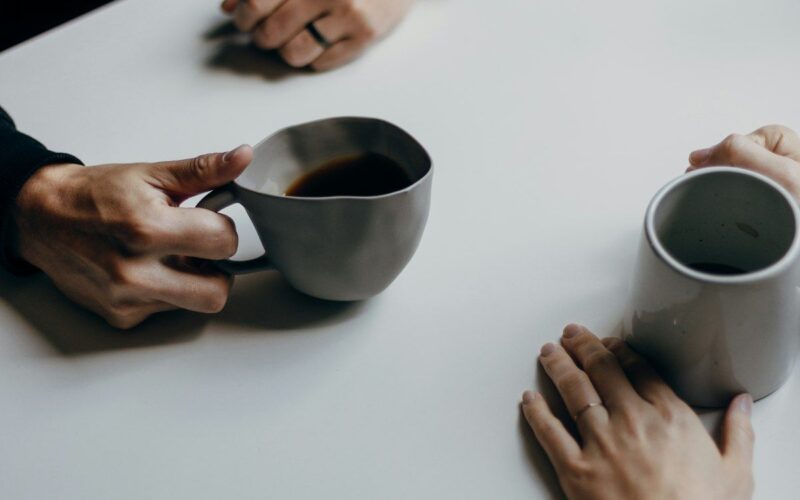 Dos personas conversando con tazas de café en una mesa, ambiente cálido y tranquilo