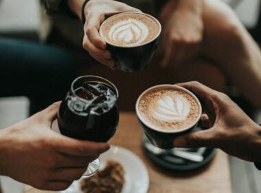 Cuatro amigos riendo y celebrando con café, ambiente social diurno y alegre