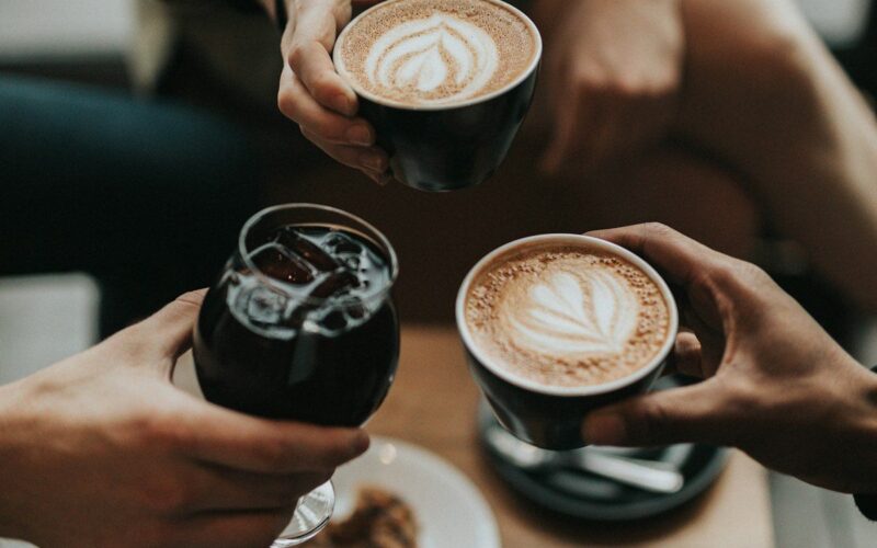 Cuatro amigos riendo y celebrando con café, ambiente social diurno y alegre