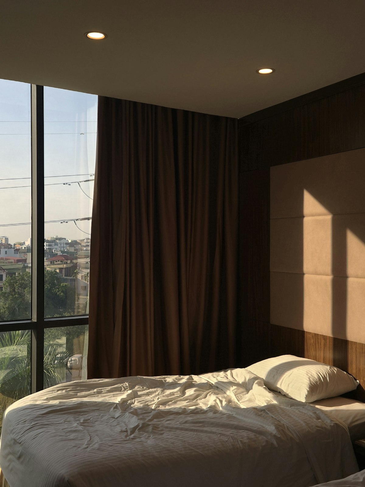 Detalle de una cama de hotel con ropa de cama neutra y luz suave de amanecer