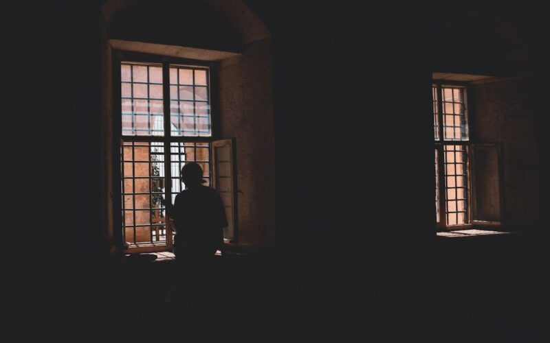 Persona sentada junto a una ventana en actitud reflexiva, luz suave de interior