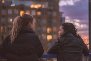 El apego seguro no es solo para el amor: cómo tu estilo afecta tus amistades Dos personas conversando de cerca junto a una ventana con luz natural, gesto de confianza