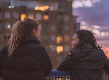 Dos personas conversando de cerca junto a una ventana con luz natural, gesto de confianza