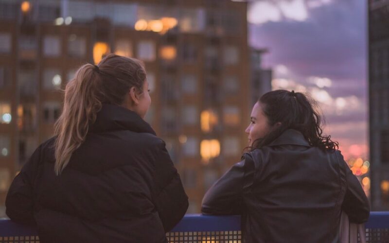 Dos personas conversando de cerca junto a una ventana con luz natural, gesto de confianza
