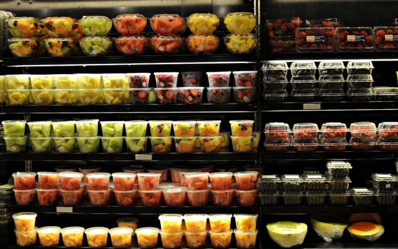 Carrito de supermercado con frutas frescas, yogur y proteínas, composición editorial