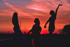 Wild health raves: por qué bailar sobrio de madrugada se volvió la nueva terapia de grupo Siluetas de personas bailando al atardecer junto al agua, ambiente sobrio y conectado