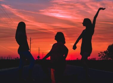Siluetas de personas bailando al atardecer junto al agua, ambiente sobrio y conectado