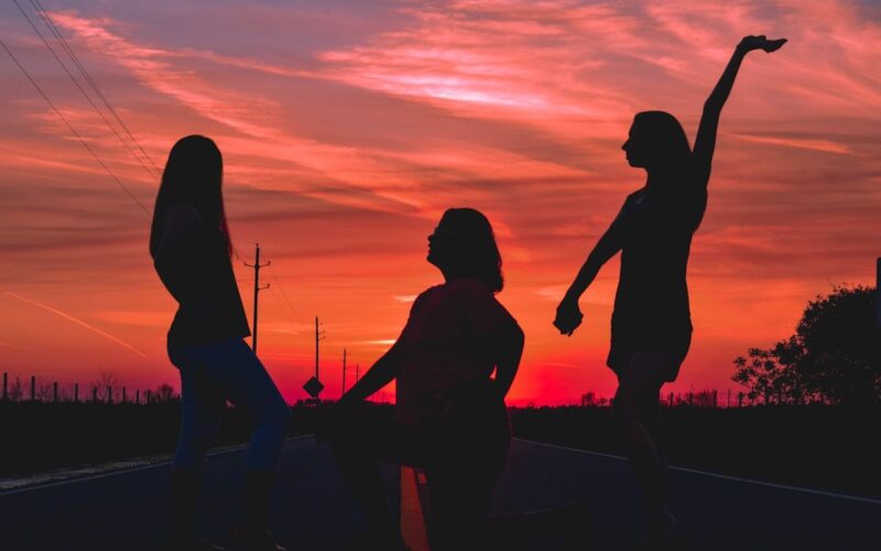 Siluetas de personas bailando al atardecer junto al agua, ambiente sobrio y conectado